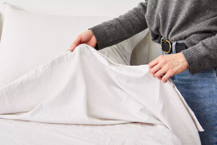 An individual arranging The Citizenry Organic Cotton Sheet Set on a bed