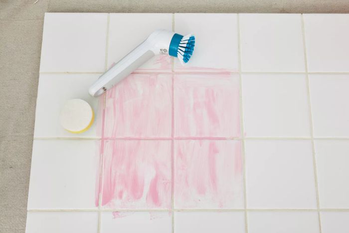 A Black+Decker Grimebuster Pro Power Scrubber Brush rests on white tile marked with red stains