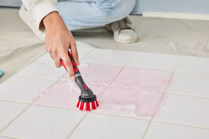 A person cleans white tile stained with red marker using a Rubbermaid Reveal Cordless Battery Powered Scrubber Home Kit
