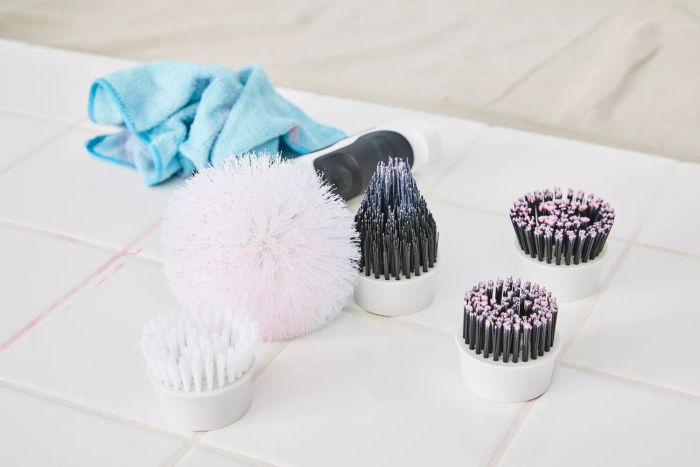Various brush attachments for the Klever Electric Spin Scrubber with 8 Brushes are placed on white tile