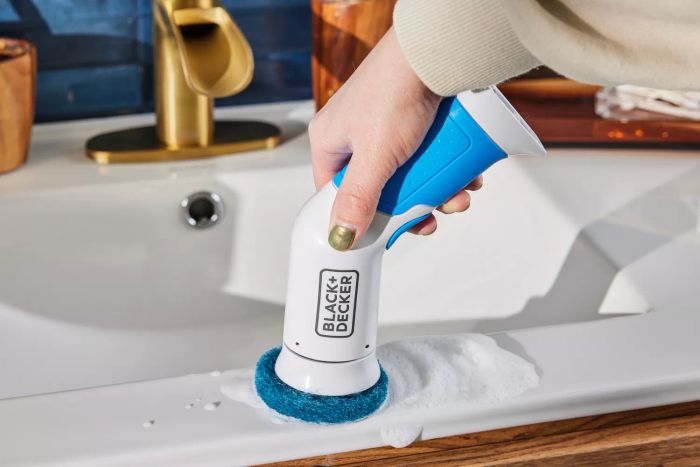 A person cleans a bathroom sink using a BLACK+DECKER Power Scrubber Brush