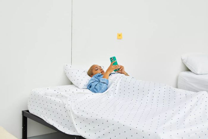 Individual lying on a bed with the California Design Den Cotton Sateen Sheet Set, holding a phone