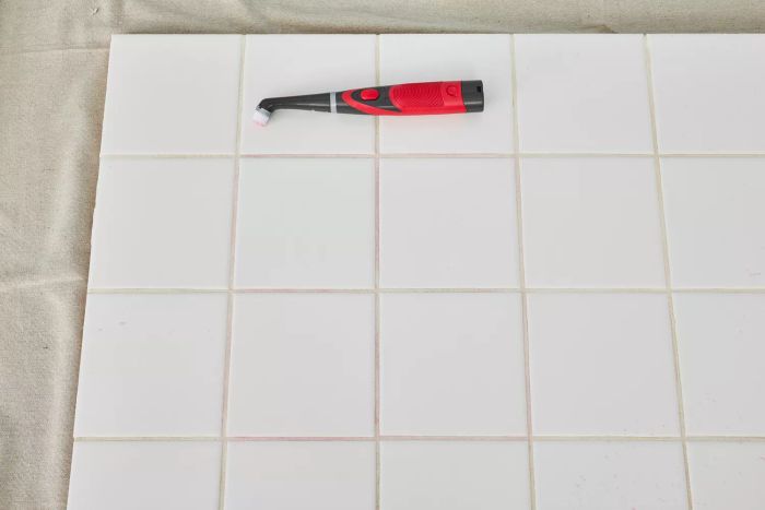 The Rubbermaid Reveal Power Scrubber is placed on pristine white floor tile