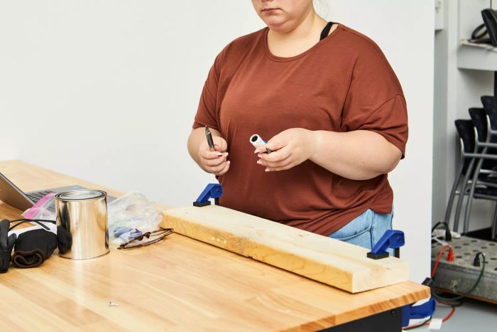 A person holding the Lenox 9-in-1 Rubber Handle Multi-Bit Screwdriver near a table with wood, a paint can, and a laptop