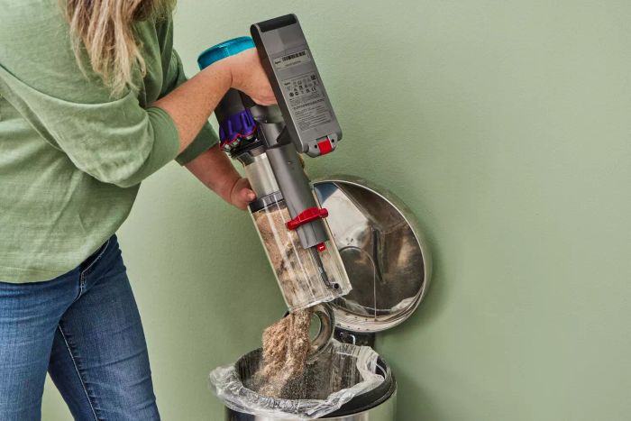 A person disposing of debris from the Dyson Gen5detect Cordless HEPA Vacuum into a trash can