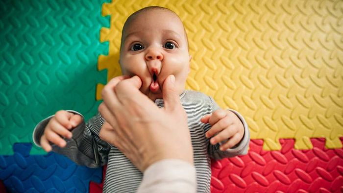 A baby dressed in gray having his cheeks pinched