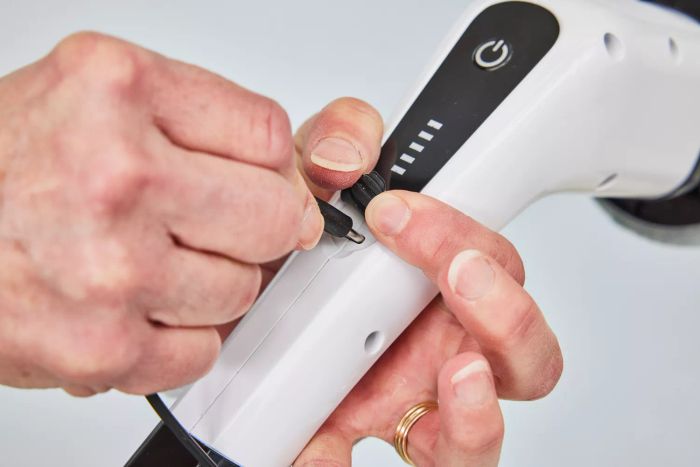 A close-up of hands plugging a charging cable into a Losuy Electric Spin Scrubber