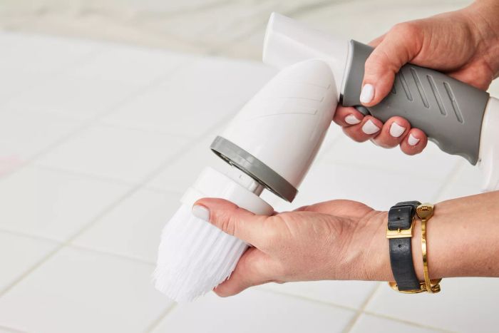 Hands hold an IEZFIX Electric Spin Scrubber above white tile