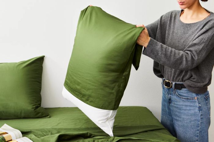 Person removing a pillowcase from a pillow featuring the Nest Bedding Sateen Organic Cotton Sheet Set
