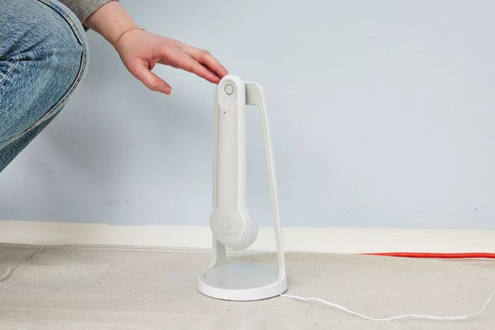 A hand interacts with a Black+Decker Grimebuster Pro Power Scrubber Brush placed on its stand
