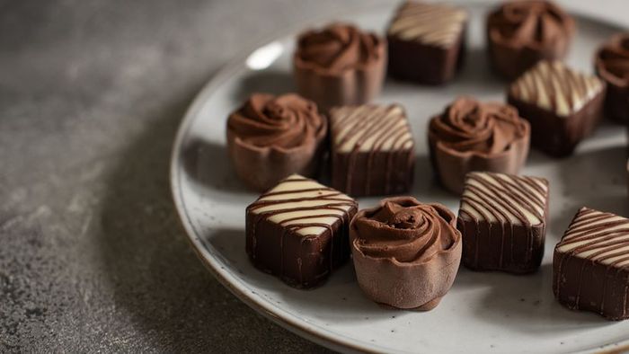 A plate of chocolate truffles, one of which has a faint white layer on its surface.