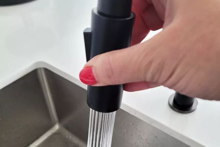 A user operating the sprayer on the Kraus KPF-2820SFACB Oletto Single Handle Pull-Down Kitchen Faucet.
