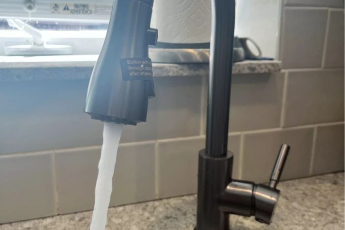 Water flowing from the Wewe Single-Handle High Arc Pull-Out Kitchen Faucet into a kitchen sink.