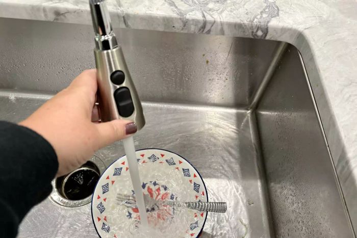 A person rinsing dishes in a sink using the sprayer of the Moen Arbor Smart Touchless Kitchen Faucet With Voice Control