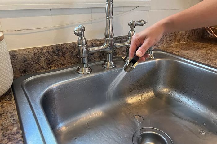 A person operating the sprayer attachment of the Kingston Brass Heritage Bridge Kitchen Faucet.