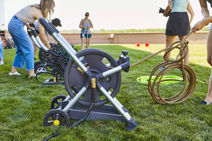 A person's hand extending the hose from the Gorilla Aluminum Zero Rust Premium Mobile Hose Reel positioned on grass