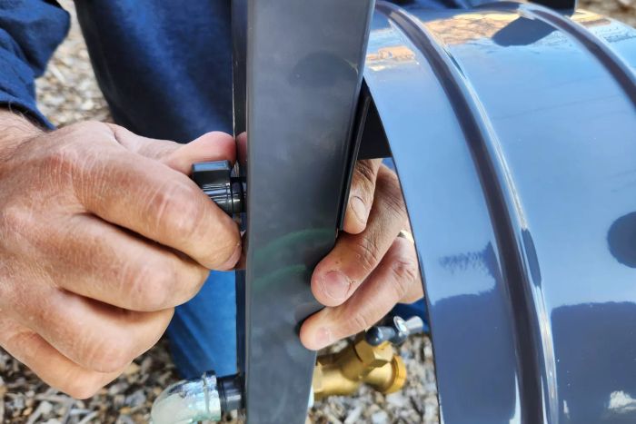 A person assembling the AQUA JOE 125 ft. Capacity Garden Hose Stand with Brass Faucet