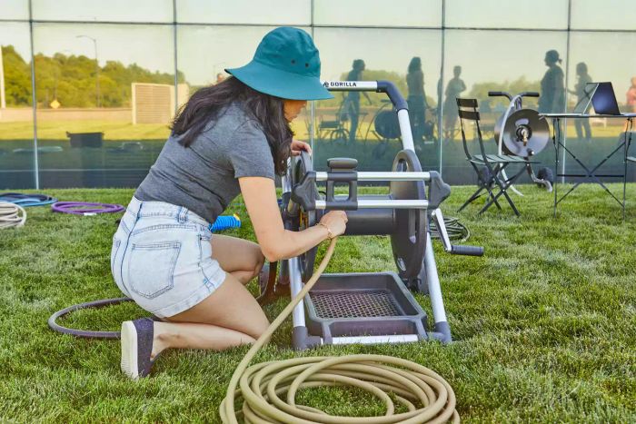 A person loading a hose into the Gorilla 200 ft. Aluminum Zero Rust Premium Mobile Hose Reel placed on a grassy surface