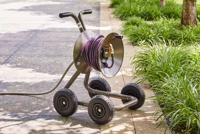 Eley Portable Garden Hose Reel Wagon positioned on a concrete surface surrounded by plants