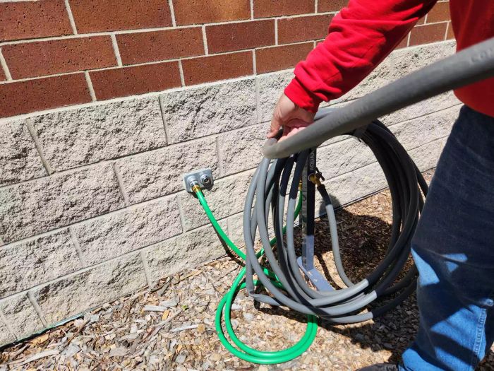 A person coiling a hose around the AQUA JOE 125 ft. Capacity Garden Hose Stand with Brass Faucet