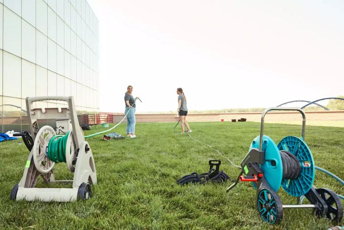 Two hose reels placed on grass, with two individuals in the distance pulling hoses from them