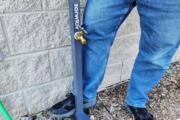 A person setting up the AQUA JOE 125 ft. Capacity Garden Hose Stand with Brass Faucet
