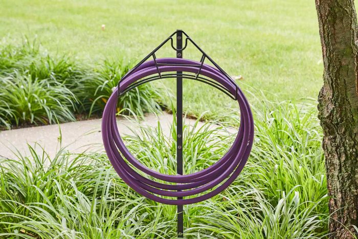A purple hose coiled on the Artigarden Freestanding Garden Hose Holder Hanger in a garden setting