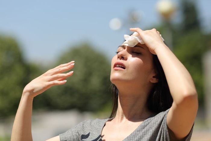 A woman is seen sweating under the direct sun, fanning herself with her hand to find some relief.