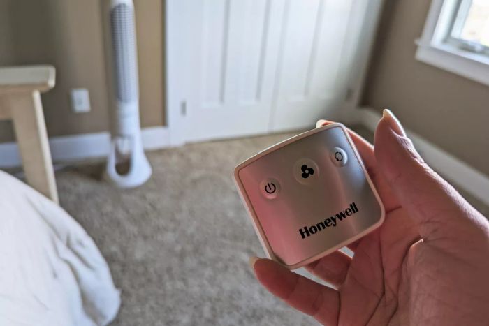 A person holding the remote control for the Honeywell QuietSet Whole Room Tower Fan