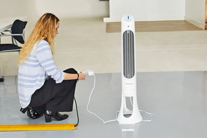 A person kneeling beside the Honeywell QuietSet Whole Room Tower Fan
