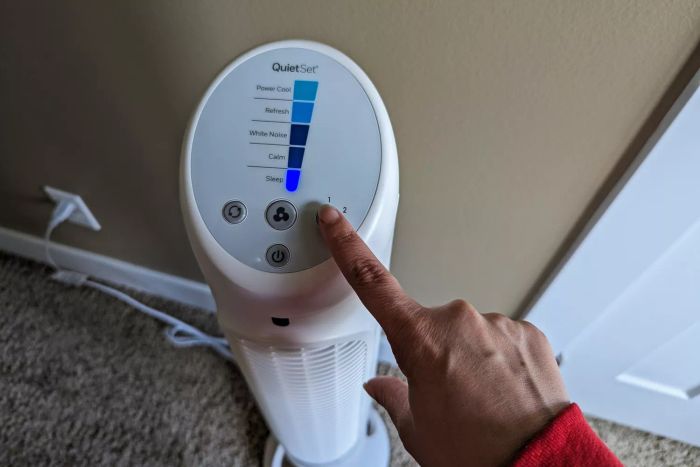 A person pressing a button on the Honeywell QuietSet Whole Room Tower Fan