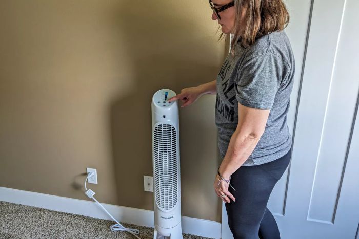 A person pressing a button on the Honeywell QuietSet Whole Room Tower Fan