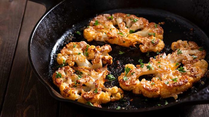 Cauliflower steaks sizzling in a skillet.