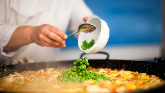 A person adding peas to a pan of paella.