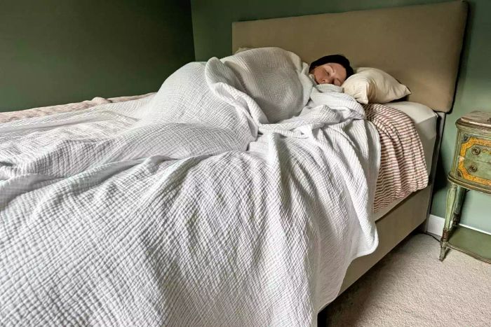 A person resting under the Bedsure 100% Cotton Muslin Throw Blanket