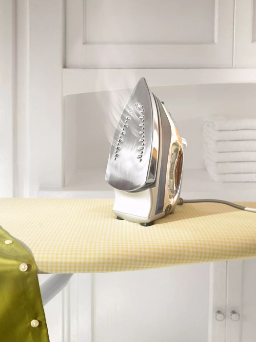 A hot iron resting on a yellow checkered ironing board.