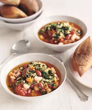 Two bowls of a hearty three-bean chili topped with vibrant spring pesto, paired with some crunchy, rustic bread on the side.