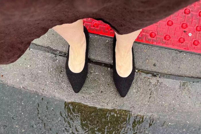 A model wearing Vivaia Aria 5° Pointed-toe Water Repellent Ballet Flats on a damp pavement