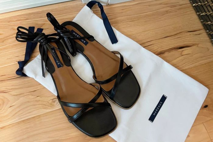 Margaux The Wrap Sandals showcased on a wooden floor alongside their storage pouch