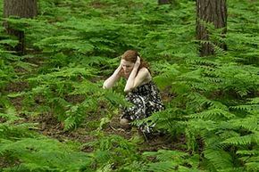 A woman stands in a field, her hands clutching her ears.