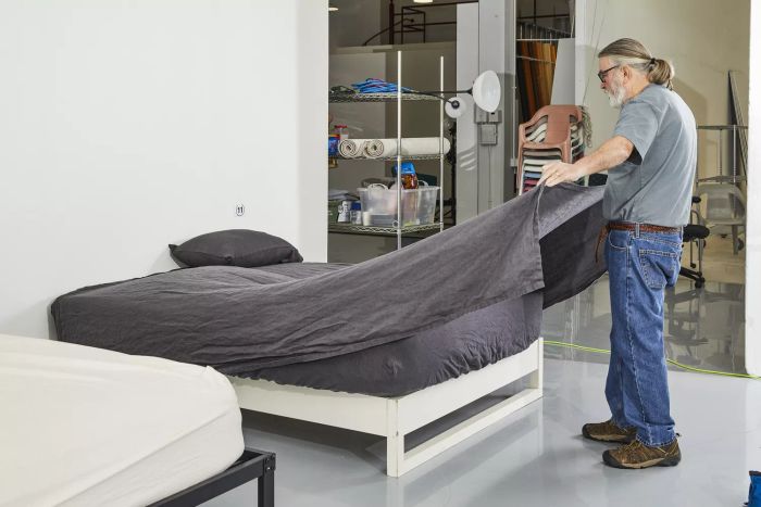 A man laying out the Quince European Linen blanket on a mattress