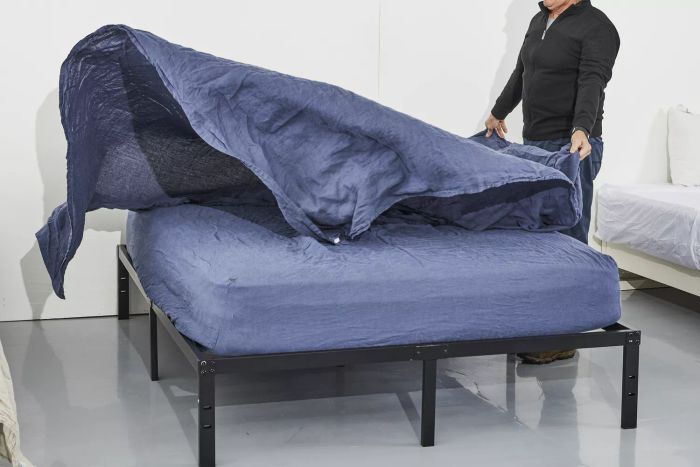 A person laying out the Citizenry Stonewashed Linen Sheet on a bed