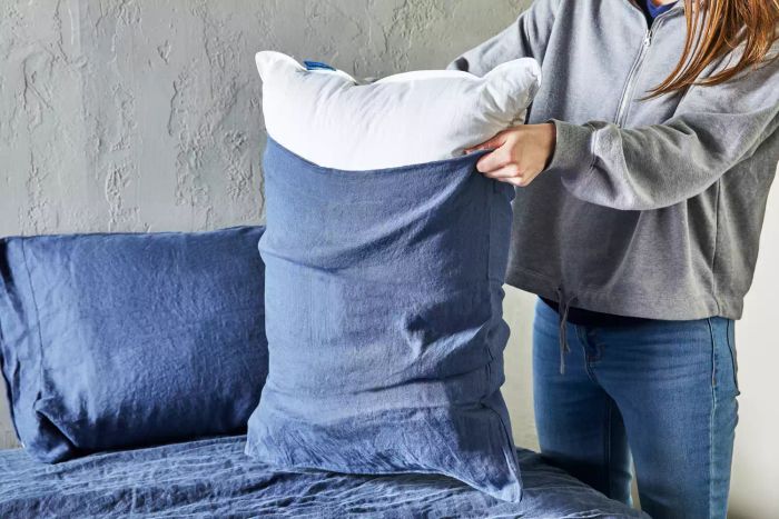 A person placing a pillow into the Citizenry Stonewashed Linen pillowcase on a bed