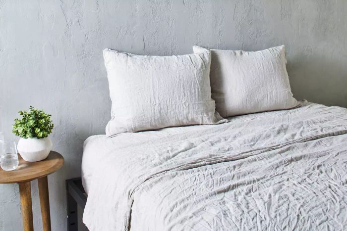 A bed adorned with Parachute Linen Sheet Set against a textured gray backdrop