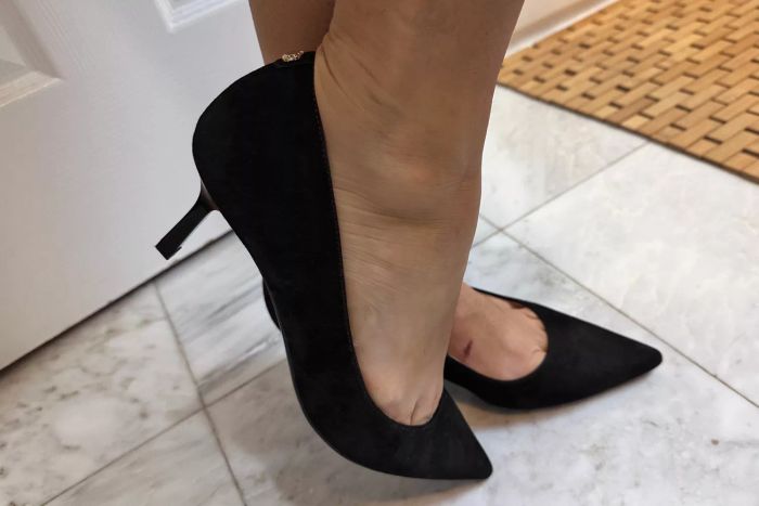 A close-up view of someone wearing Nine West Kuna 9x9 Pointy Toe Pumps on tile flooring