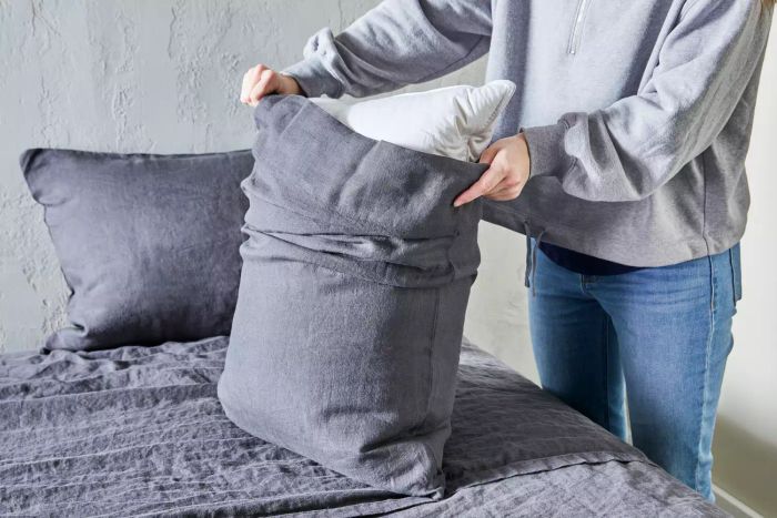 A person placing a pillow into the Quince European Linen pillowcase on a bed