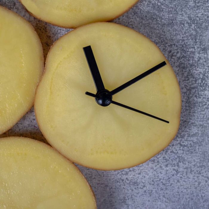 A potato slice fashioned into a clock, set against a gray backdrop