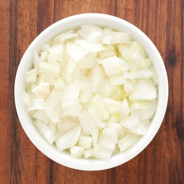 A white onion being diced in a bowl.