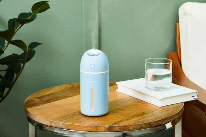 The Hey Dewy Wireless Facial Humidifier releasing steam on a side table