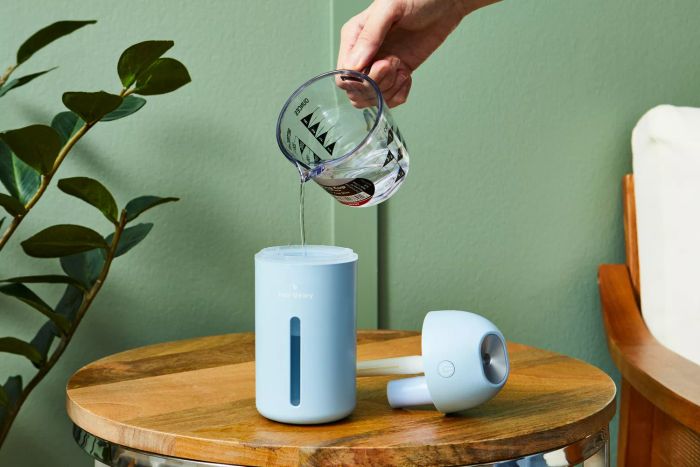 A hand is pouring water into the Hey Dewy Wireless Facial Humidifier